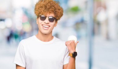 Seyir ve başparmak yanında yukarıyı mutlu yüz ile gülümseyen güneş gözlüğü takıyor afro saçlı Genç yakışıklı adam.