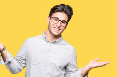 Gülen iki elle gösterilen açık avuç içi, sunma ve karşılaştırma ve denge reklam arka plan üzerinde gözlük takan genç yakışıklı adam izole