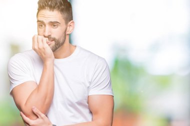 Stresli ve gergin elle çivi ısırma ağzına bakarak izole arka plan üzerinde rahat beyaz t-shirt giyen genç adam. Anksiyete sorunu.