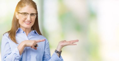 Hayret ve el ile sunulması ve parmak ile işaret ederken kameraya gülümseyen izole arka plan üzerinde gözlük güzel orta yaş olgun iş kadını.