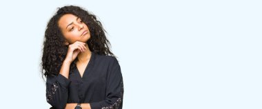 Kıvırcık saçlı zarif el ile çene düşünme hakkında soru, dalgın ifade üzerine elbise genç güzel kız. Düşünceli yüzüyle gülümsüyor. Şüphe kavramı.