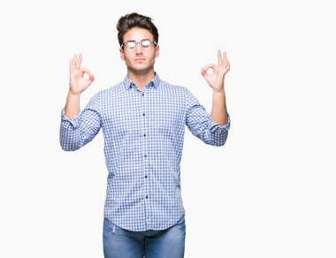 Genç yakışıklı adam gözlük izole arka plan üzerinde dinlenmek ve gülümseyen gözlerle parmak ile meditasyon jest yapıyor kapalı. Yoga kavramı.