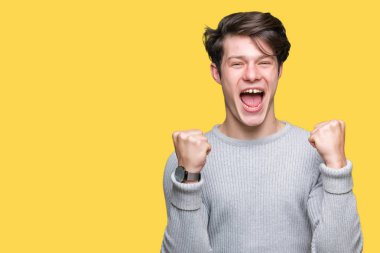 Yakışıklı delikanlı izole arka plan üzerinde kutluyor kış kazak giyen şaşırttı ve başarı için kaldırdı kollarını açarak hayret ve gözleri açık. Kazanan kavramı.