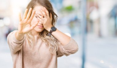 Sweatershirt üzerinde giyen genç güzel sarışın kadın izole elleriyle gözlerini kapsayan arka plan ve dur jest ile acı ve korku ifadesi. Utandım ve negatif kavramı.