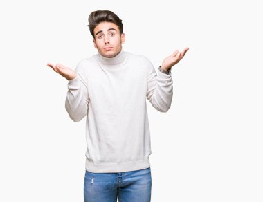 Üzerinde boğazlı kazak giyen genç yakışıklı adam arka plan clueless ve şaşkın bir ifadeyle kollar ve eller kaldırdı izole. Şüphe kavramı.