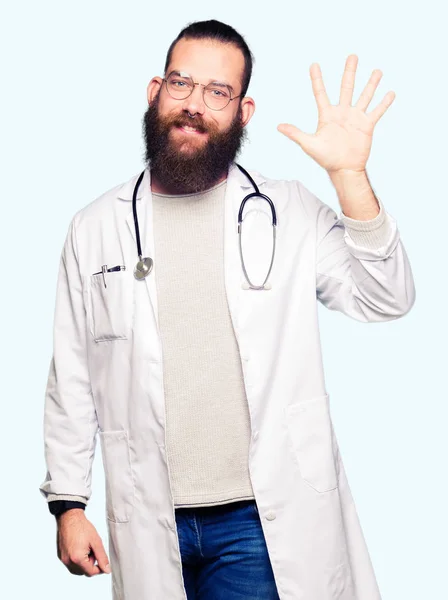 若いブロンド医師男性でひげを示す医療の着用のコートと自信を持って 幸せな笑みを浮かべて 指で上向きナンバーファイブ — ストック写真
