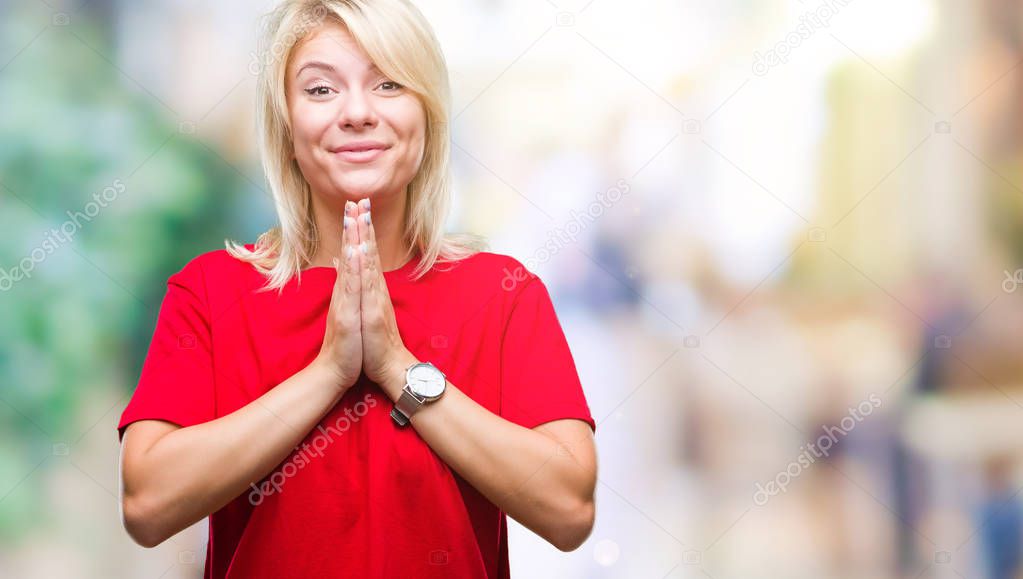 Young beautiful blonde woman wearing red t-shirt over isolated background praying with hands together asking for forgiveness smiling confident.