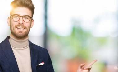 Kameraya bakarak yan el ve parmak ile işaret yüzünde, kocaman bir gülümseme ile gözlük takan genç yakışıklı iş adamı.