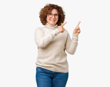 Boğazlı kazak ve gözlük gülümseyen ve iki elleri ve parmakları ile tarafına işaret kamera bakarak izole arka plan üzerinde giyen güzel orta ager üst düzey kadın.