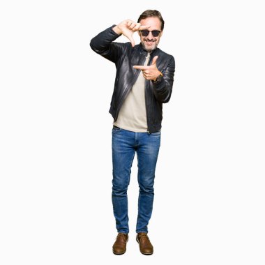 Güneş gözlüğü ve siyah deri ceket giyen orta çağ yakışıklı adam mutlu yüz ile eller ve parmaklar ile çerçeve yapma gülümseyen. Yaratıcılık ve Fotoğrafçılık konsepti.
