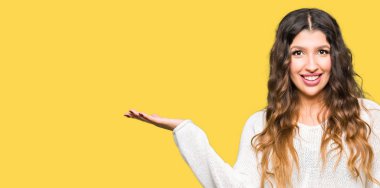 Beyaz kazak giyen genç güzel kadın neşeli sunan gülümseyerek ve kameraya bakarak avuç içi ile işaret.