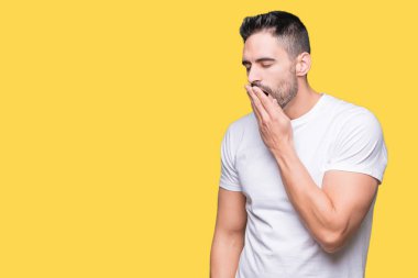 İzole arka plan üzerinde rahat beyaz t-shirt giyen genç adam el ağzıyla kapsayan yorgun esneme sıkılmış. Restless ve uyku hali.