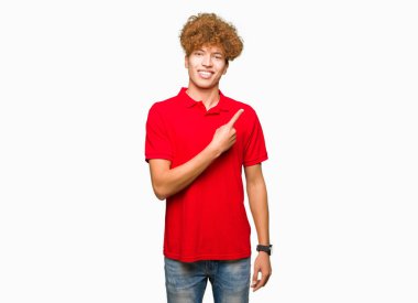 Kırmızı t-shirt neşeli bir gülümseme ile el ve parmak kadar yan yüzünde mutlu ve doğal ifade ile işaret yüz giyen afro saçlı Genç yakışıklı adam
