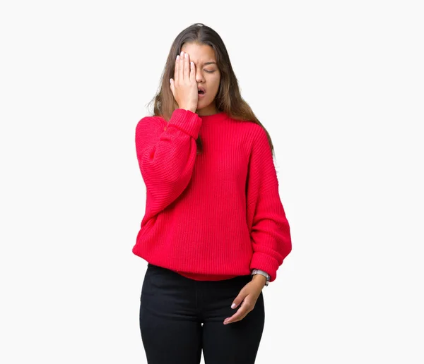 年轻美丽的黑发女人穿着红色的冬季毛衣在孤立的背景打哈欠累覆盖半脸 眼睛和嘴巴用手 脸在痛苦中受伤 — 图库照片
