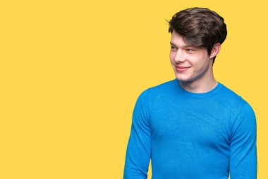 Genç yakışıklı adam uzak tarafına yüzünde, doğal ifade gülümseme ile seyir izole arka plan üzerinde mavi kazak giyiyor. Kendine güvenen gülüyor.