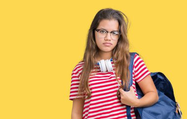 Yüzünde ciddi bir ifade ile izole arka plan üzerinde kulaklık ve sırt çantası giyen genç güzel esmer öğrenci kadın. Basit ve doğal kameraya bakıyor.