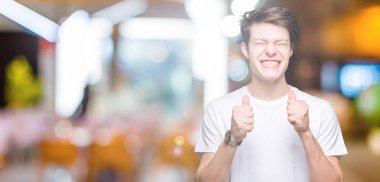 Zafer kutluyor gülümseyen izole arka kolları olan başarı için heyecan üzerinde rahat beyaz t-shirt giyen genç yakışıklı adam kaldırdı. Kazanan kavramı.