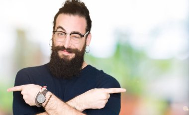 Uzun saç ve sakal giyen genç hipster adamla işaret parmakları ile her iki taraf için gözlük, farklı yönde katılmıyorum