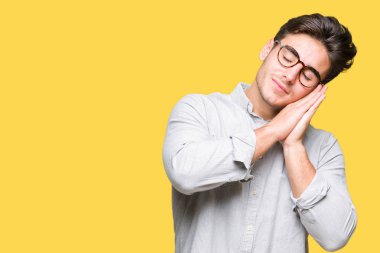 Uyku yorgun hayal ve ellerle birlikte poz ile kapalı gözler gülümseyen izole arka plan üzerinde gözlük takan genç yakışıklı adam.