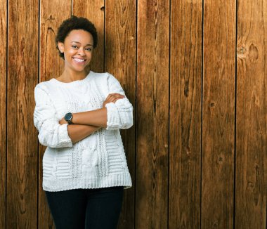 Üzerinde kazak giyen güzel genç Afro-Amerikan kadın arka plan ile mutlu yüz gülümseyerek kameraya seyir silah geçti izole. Olumlu bir kişi.