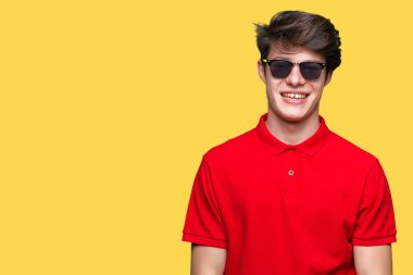 Genç yakışıklı adam yüzünde mutlu ve güzel bir gülümseme ile izole arka plan üzerinde güneş gözlüğü takıyor. Şanslı kişi.