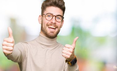Onaylama gülümseyerek el, başparmak ile pozitif jest yapıyor ve başarı için mutlu gözlüklü genç yakışıklı iş adamı. Kamera, kazanan jest arıyorsunuz.