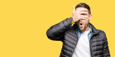 Yakışıklı adam kış ceket yüz ve gözler el ile kapsayan şok bakmak giyen mahcup ifadeyle parmaklarımın arasından bakan.