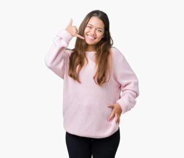 İşin gülümseyen izole arka plan üzerinde pembe kış kazak giyen genç güzel esmer kadın telefon hareketi ile el ve parmak telefonda konuşuyor gibi. Kavramları iletişim.