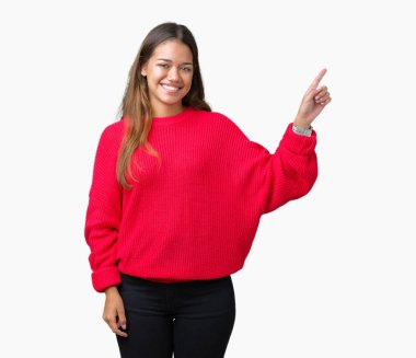 Kameraya bakarak yan el ve parmak ile işaret yüzünde kocaman bir gülümseme ile izole arka plan üzerinde kırmızı kış kazak giyen genç güzel esmer kadın.