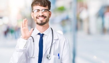 Hastane kat izole arka plan Waiving mutlu selam söyleyerek üzerinde ve gülümseyen, dostça karşılama jest giyen adam genç doktor