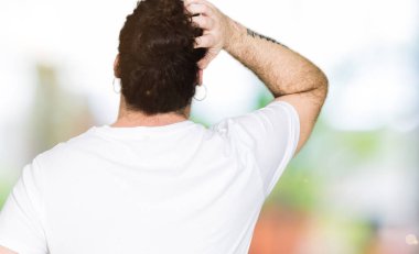 Uzun saç ve sakal geriye doğru elle kafasında şüphe hakkında düşünme casual beyaz t-shirt giyen genç hipster adamla