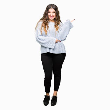 Kameraya bakarak yan el ve parmak ile işaret yüzünde, kocaman bir gülümseme ile kış kazak giyen genç güzel kadın.