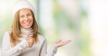 Üzerinde kış kazak ve şapka giyen güzel orta yaş kadın arka plan gösteren palm el ve iş tamam jestle başparmak yukarıya, mutlu ve neşeli gülümseyen izole