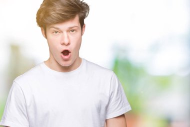 Casual beyaz giyen genç yakışıklı adam şüpheci ve alaycı, t-shirt üzerine şok karşısında izole arka plan açık ağız ile şaşırttı.