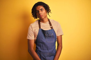 Afro Amerikan barista adam dreadlocks yüzünde ciddi ifade ile izole sarı arka plan üzerinde önlük giyen. Kameraya basit ve doğal bir bakış.