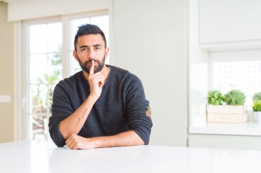 Yakışıklı İspanyol adam evde rahat kazak giyen dudaklarında parmak ile sessiz olmak isteyen. Sessizlik ve gizli kavram.