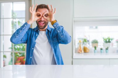 Yakışıklı adam evde dürbün dil dışarı sopa gibi ok jest yapıyor, gözleri parmaklardan bakarak. Çılgın ifade.