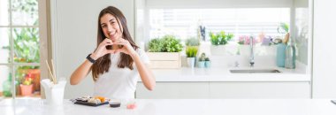 Doğumdan asya suşi yiyen güzel genç kadının geniş açılı resmi, kalp sembolü ve şeklini elleriyle göstererek sevgiyle gülümsüyor. Romantik kavram.