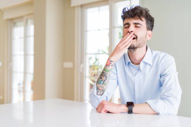 Beyaz masada oturan genç iş adamı sıkılmış esneme yorgun el ile ağız kapsayan. Huzursuz ve uykululuk.