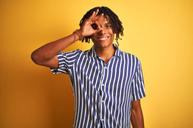 Dreadlocks ile rahat çizgili t-shirt giyen afro adam izole sarı arka plan üzerinde el gülümseyerek ok jest yapıyor, mutlu yüz ile parmakları ile bakan göz.