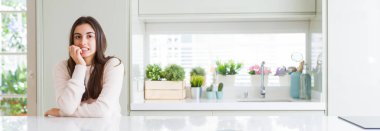 Güzel genç kadın evde beyaz masaya oturan geniş açı resim stresli ve gergin elle çivi ısırma ağzına arıyorum. Anksiyete sorunu.