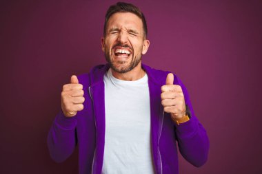 Mor izole arka plan üzerinde rahat spor sweatshirt giyen genç fitness adam kollarını kaldırdı ve gözleri gülümseyerek zafer kutlayan kapalı başarı için heyecanlı. Kazanan kavramı.