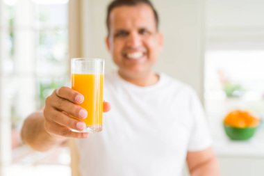 Orta yaş adam ayakta mutlu bir yüz ile evde portakal suyu bir bardak içme ve dişleri gösteren kendinden emin bir gülümseme ile gülümseyerek