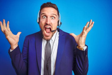 Genç yakışıklı operatör adam mavi izole arka plan üzerinde çağrı merkezi kulaklık giyen deli kutluyor ve kollarını kaldırdı ve açık gözleri heyecan çığlık ile başarı için hayran. Kazanan kavramı