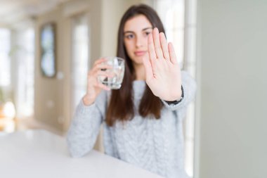 Güzel genç kadın ciddi ve kendinden emin ifade, savunma jesti ile dur işareti yapıyor açık el ile su taze bir bardak içme