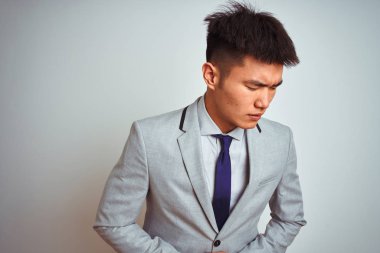 Gri ceket giyen ve kravat takan Asyalı çinli işadamı, midesinde el ile izole edilmiş beyaz arka plan üzerinde durarak hazımsızlık, acı lı hastalık hissi. Ağrı kavramı.