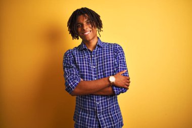 Izole sarı arka plan mutlu yüz kameraya bakarak çapraz kolları ile gülümseyen üzerinde duran rahat gömlek giyen dreadlocks ile Afro adam. Pozitif kişi.