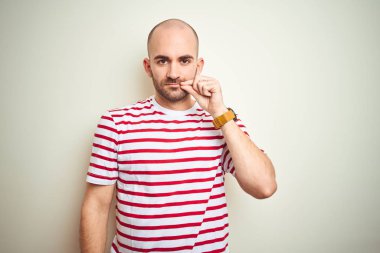 Beyaz izole arka plan ağız ve dudaklar üzerinde rahat çizgili kırmızı t-shirt giyen sakallı genç kel adam parmakları ile zip olarak kapattı. Gizli ve sessiz, tabu konuşma