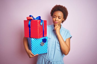 Afro-Amerikan kadın pembe izole arka plan üzerinde doğum günü hediyeleri tutan ciddi yüz soru hakkında düşünme, çok karışık fikir
