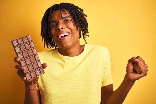Afro Americký Muž Dredy Pojídáním Čokoládového Baru Přes Izolované Žluté — Stock fotografie
